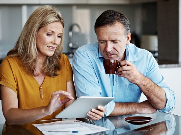 woman and man sit at a table and look at a tablet and papers together