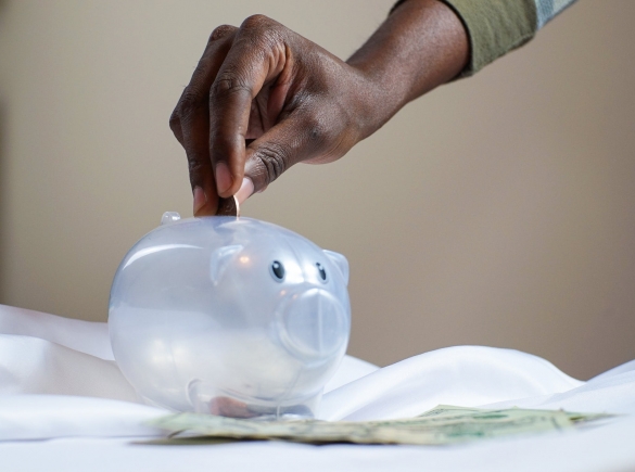 photo shows a hand putting a coin in a piggy bank