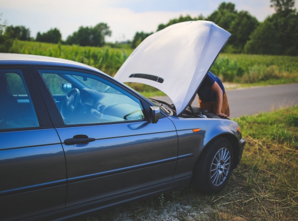 man looking under hood of car on the side of the road