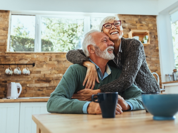 An elderly couple embrace in their kitchen.