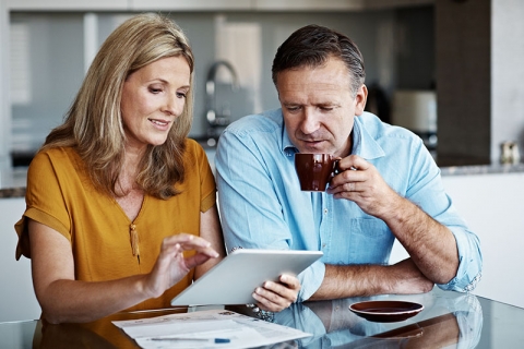 woman and man sit at a table and look at a tablet and papers together