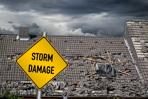 sign that says storm damage sits in front of damaged roof